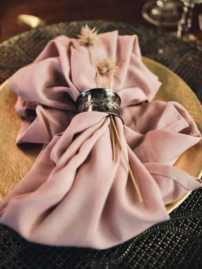 Latex napkin in a metal ring decorated with dried flowers on a gold background as part of a wedding table