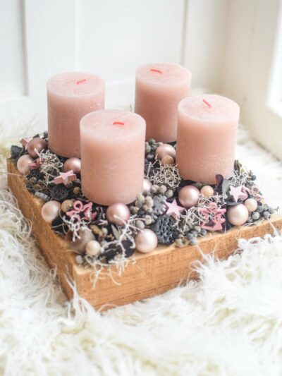 Christmas candle holder with four pink candles on a square wooden base decorated with natural decorations in grey and pink color