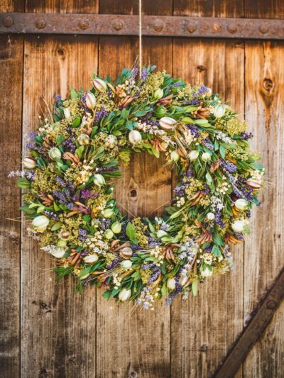 Natural hanging wreath from greenery and purple and white dried flowers with lavender hung on a wooden door.