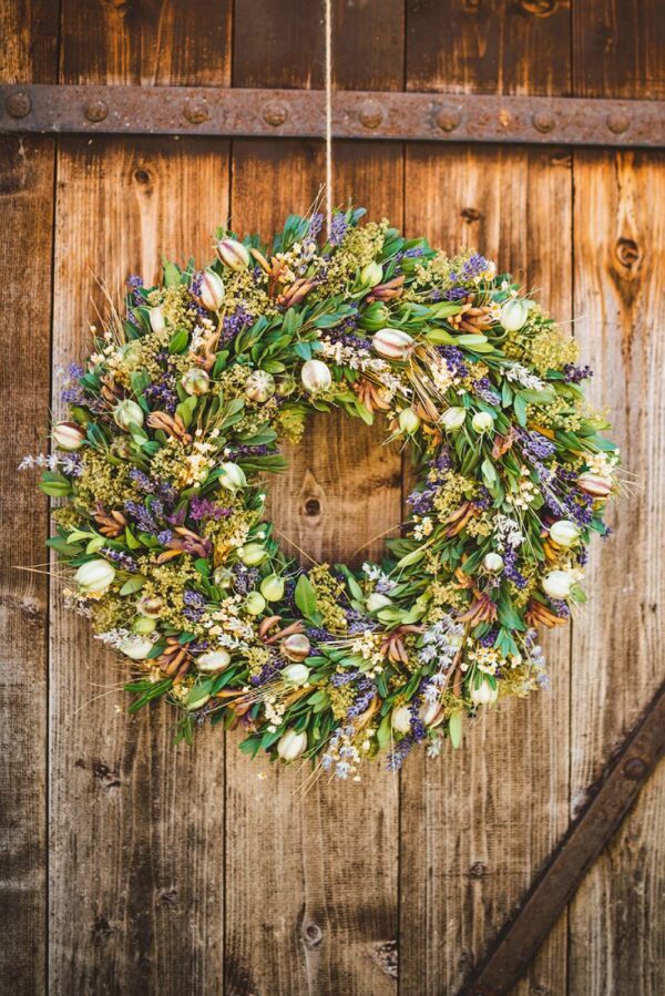 Natural hanging wreath from greenery and purple and white dried flowers with lavender hung on a wooden door.