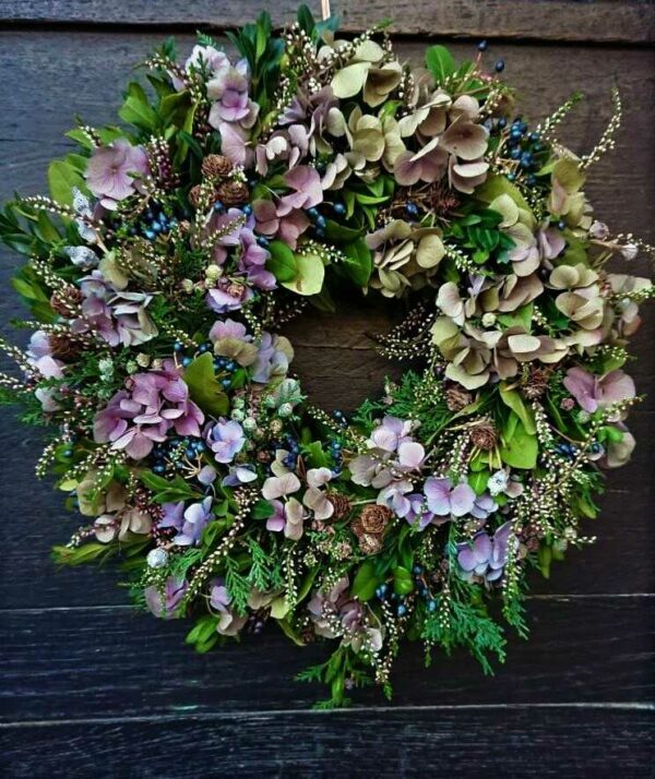 Natural wreath to hang in green and purple colors from hydrangea, heather, thuja, cones, Viburnum.
