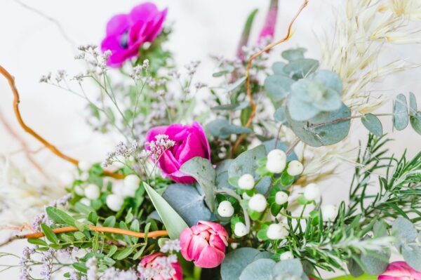 Kytice uvázaná z fialových květů sasanky a rozrazilu, statice, růžových tulipánů, bílých bobulí třezalky, zeleně, sušeného ovsa a proutků kroucené vrby.
