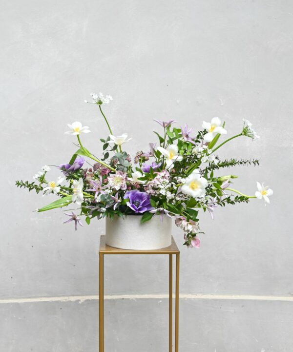 Jarní květinový box s čerstvými jarními květinami, eukalyptem a myrtou v bílém obalu na zlatém podstavci.