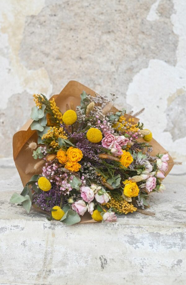 Colourful dried bouquet tied with dried flowers and greenery in a paper sleeve.